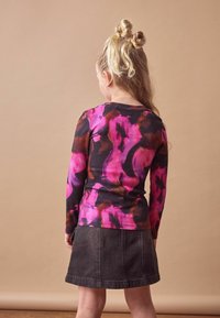 Langarmshirt in een roze en zwart abstract patroon, gecombineerd met een donkerdenim rok. Gekreukt ribbenstof met een getailleerd ontwerp.