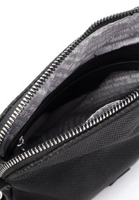 Portafoglio nero con zip, esterno perforato, hardware argentato e fodera interna grigia a motivo con testo ripetuto. Design compatto e texture interessante.