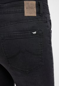 Czarne dżinsy z denimu z skórzaną metką marki z napisem "MUSTANG" na pasku. Na tylnej kieszeni znajduje się małe logo w kształcie konia.