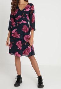 Bloemige jurk met een marineblauwe achtergrond, voorzien van grote roze bloemen, een V-halslijn, driekwart belmouwen en een losse pasvorm.