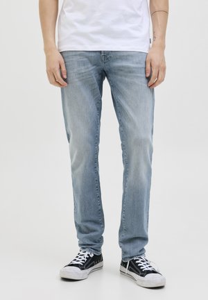 Jeans de mezclilla azul claro con corte recto, costuras detalladas y textura desgastada, combinados con zapatillas de lona negras.