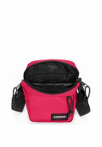 Borsa a tracolla rossa in nylon con chiusura con zip, interno nero e tracolla regolabile. Presenta una patch con logo e una superficie testurizzata.