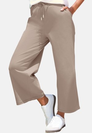 Beige wide-leg cropped pants with drawstring waist, worn with white sneakers; one hand in pocket, standing against plain background.