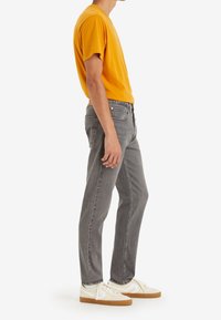 Jeans rectos grises, combinados con una camiseta de manga corta amarilla brillante y zapatillas blancas con suelas de goma. Diseño limpio, ajuste casual.