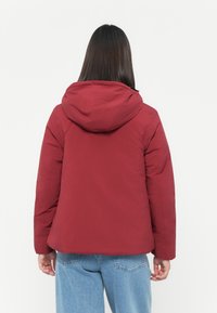 Rote gepolsterte Jacke mit Kapuze, die eine glatte Textur und eine lockere Passform hat. Entwickelt für Wärme und Komfort.