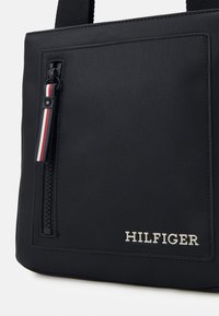 Borsa nera con texture, dotata di tasca con zip e tirazip a strisce tricolori, logo impresso e design strutturato. Materiale resistente e finitura elegante.