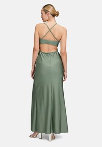 Grünes Satin-Maxi-Kleid mit überkreuzten Trägern, offener Rückseite und gepunkteter Textur. Fließendes Design reicht bis zum Boden mit einer taillierten Silhouette.