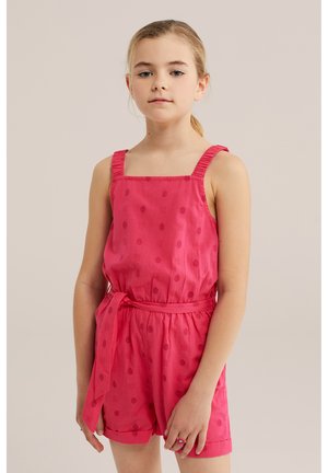 Noor blondide juustega tüdruk hobusesabaga, kandes varrukateta roosat kombinesooni sobiva vöö ja õrna täpilise mustriga.