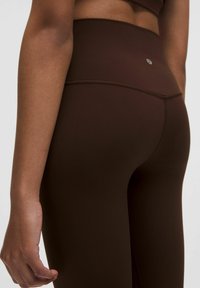 Brown high-waisted leggings made of smooth, stretchy fabric, featuring a fitted design and a small logo tag at the back waistband.