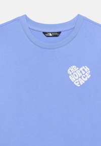 Ανοιχτό μοβ μπλουζάκι με στρογγυλή λαιμόκοψη, με λευκό λογότυπο σε σχήμα καρδιάς "The North Face" στο αριστερό στήθος και μαύρη ετικέτα μάρκας μέσα στο γιακά.