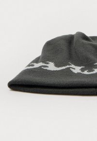Cappello beanie in maglia grigio scuro con motivo di cavallo che corre in bianco vicino al bordo, posato su uno sfondo bianco.