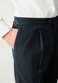 Navy pinstripe trousers with a pleated front, made of fabric with a smooth texture. Features a silver buckle accent on the waistband.