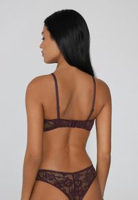 Burgunderfarbener Spitzen-BH mit verstellbaren Trägern, der mit Blumenmustern und einem Haken- und Ösenverschluss versehen ist. Dazu passende Spitzenunterwäsche.