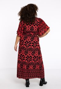 Rød maxikjole med blomsterprint, sorte detaljer, korte flagrende ærmer og en markeret talje. Afsluttet med en nederdel der når midt på læggen. Sorte støvler.