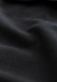 Tessuto nero con una consistenza liscia, che presenta pieghe sottili. Il materiale appare denso e opaco, senza schemi o accenti visibili.