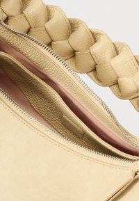 Borsa a mano in pelle beige con manico intrecciato, aperta per mostrare una fodera rosa e un interno suddiviso in scomparti. Superficie esterna texturizzata.