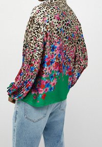 Silmänystävän silkkinuttu, jossa leopardikuvio ja värikkäitä kukka-aiheisia yksityiskohtia. Vihreä pohja, laskostetut hihat ja rento istuvuus.