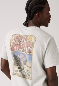 Camiseta de algodão cinza com um gráfico retro da Levi Strauss & Co. nas costas, retratando cowboys e cavalos com texto e detalhes coloridos.