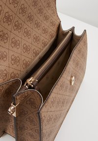 Ruskea teksturoitu käsilaukku geometrisella kuviolla, jossa on vetoketjullinen lokero ja kullanväriset metalliosat.