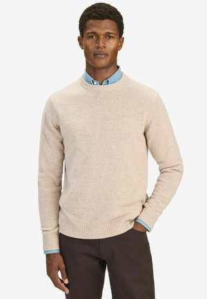 Beige strikket sweater med rund halsudskæring, ribbede manchetter og kant. Sammen med en lys blå skjorte med knapper under.