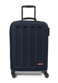 Maleta rígida de color navy con ranuras verticales, asa retráctil, cuatro ruedas y un parche del logo negro de Eastpak en la parte delantera.