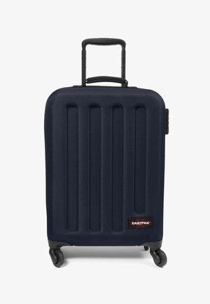 Maleta rígida de color navy con ranuras verticales, asa retráctil, cuatro ruedas y un parche del logo negro de Eastpak en la parte delantera.