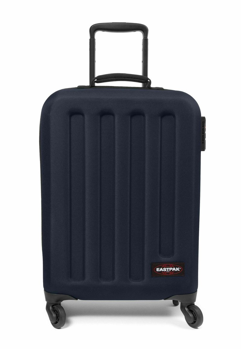 Maleta rígida de color navy con ranuras verticales, asa retráctil, cuatro ruedas y un parche del logo negro de Eastpak en la parte delantera.