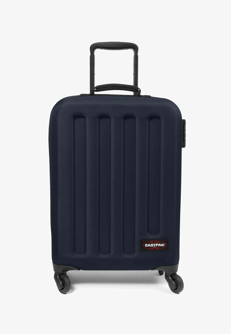 Maleta rígida de color navy con ranuras verticales, asa retráctil, cuatro ruedas y un parche del logo negro de Eastpak en la parte delantera.