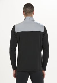 Langærmet træningsskjorte med en sort krop og en grå yoke ved skuldrene, glat tekstur og slankt design til aktivt brug.