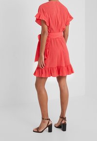 Korálové šaty s volánovými rukávy a lemem, s páskem v pase, z texturované látky, spárované s hnědými sandály na řemínky a blokové podpatky.