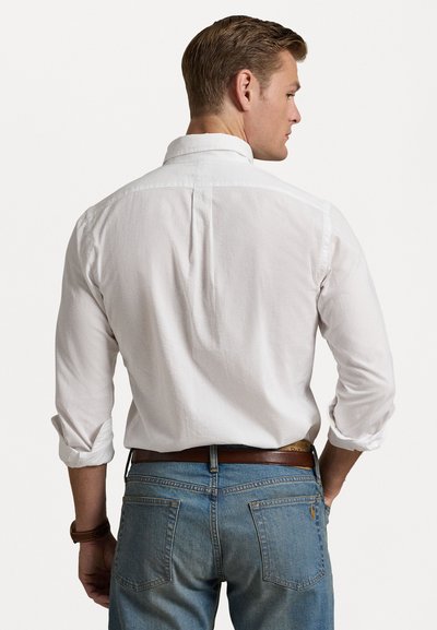 Camisa branca com botões e mangas dobradas, tecido texturizado, yoke nas costas e um corte relaxado, combinada com jeans azul e um cinto castanho.