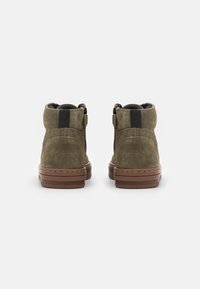 Zielono-oliwkowe zamszowe botki za kostkę z brązową gumową podeszwą, z zaokrąglonym noskiem, dwoma bocznymi zamkami błyskawicznymi i materiałową wyściółką.