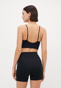 Soutien-gorge de sport noir sans couture avec bretelles réglables, associé à un short noir taille haute. Texture lisse avec des détails de couture minimaux.