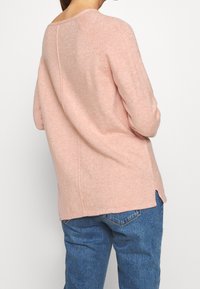 Maglione a maglia morbida di un rosa chiaro, con scollo rotondo, maniche lunghe e un delicato dettaglio sulle cuciture. Presenta spacchi laterali all'orlo.