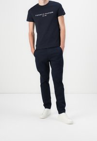 Camiseta de algodón azul marino con "TOMMY HILFIGER EST. 1985" impreso en blanco. Combinada con pantalones ajustados azul marino y zapatillas blancas. Conjunto casual.