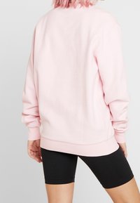 Jasnoróżowa bluza o luźnym kroju, z prążkowanymi mankietami i obrębem, z gładką fakturą. Nosi się ją na czarne szorty.