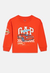 Jasnofarebná oranžová košeľa s dlhým rukávom s červeným pretekárskym autom, nápisom "GAP" a logami Hot Wheels na prednej strane a na ľavom rukáve.