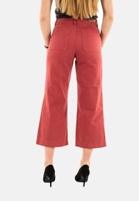 Pantaloni larghi a culotte rossi in cotone, con due tasche posteriori e una cintura in vita, abbinati a scarpe col tacco nere.