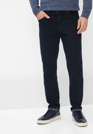 Dunkelblaue Denim-Jeans mit geradem Bein, Fronttaschen und einer subtilen Textur, kombiniert mit marineblauen Sneakers mit einer weißen Sohle.