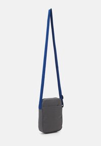 Borsa a tracolla grigia in tessuto con una tracolla blu. Forma rettangolare, superficie liscia, dotata di una tasca frontale e tracolla regolabile.