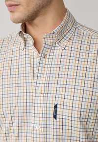 Camisa de botones en tejido ligero, con un patrón de cuadros multicolor en azul, naranja y crema. Incluye una pequeña etiqueta de la marca en el pecho.