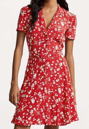 Femme portant une robe rouge à manches courtes boutonnée avec des imprimés nautiques et floraux blancs et une ceinture en tissu assortie à la taille.