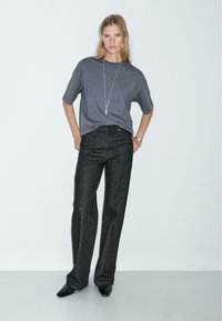 T-shirt grigio a maniche corte abbinato a jeans in denim scuro a vita alta. Outfit completato con una lunga collana e scarpe nere a punta.