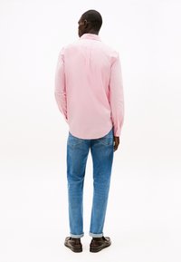 Lyserosa, langermet skjorte med spiss krage, kombinert med blå denimjeans. Skjorten har en sentral bakfold og knappede mansjetter.