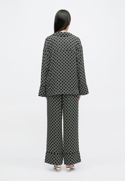 Δύο κομμάτια ντύσιμο με γεωμετρικό σχέδιο σε μαύρο και άσπρο. Το χαλαρό μπουφάν έχει μακριά μανίκια, ενώ τα παντελόνια είναι φαρδιά.