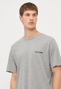 Szara koszulka z krótkim rękawem, wykonana z miękkiego materiału, z okrągłym dekoltem i małym czarnym logo "JACK & JONES" na lewej piersi.