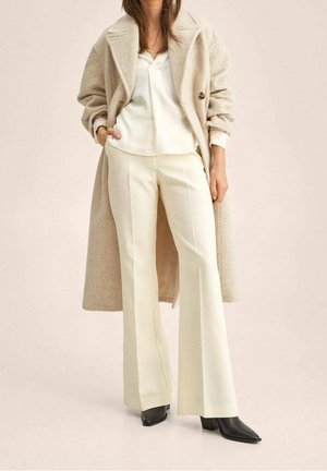 Cappotto di lana beige, blusa di raso bianca, pantaloni a campana color crema, stivali neri a punta. Tessuti texture e design classico. Vestibilità sartoriale.