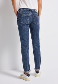 Jeans de mezclilla azul oscuro con un corte recto, diseño de cinco bolsillos, puños doblados y un parche de cuero en la cinturilla. Zapatillas blancas puestas.