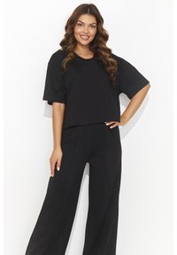 Czarny krótki t-shirt z krótkim rękawem, w zestawieniu z szerokimi czarnymi spodniami. Oba wykonane z miękkiego materiału, mają luźny krój i subtelne szwy.