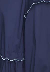 Un tessuto blu navale dalla trama liscia presenta un bordo ondulato in azzurro chiaro lungo le cuciture, mostrando un dettaglio di design arricciato.